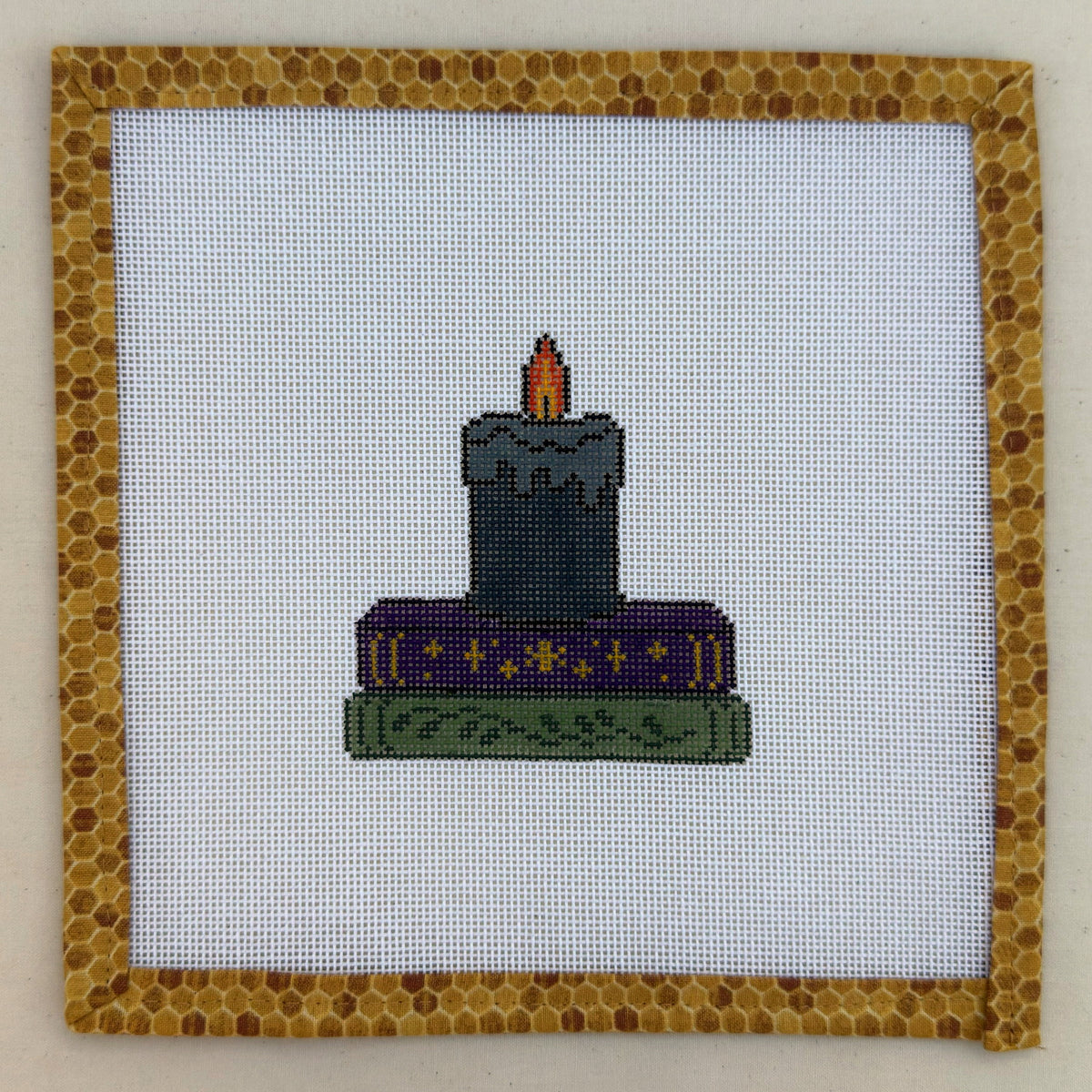 Hand-painted needlepoint canvas of a lit black candle on a stack of spellbooks