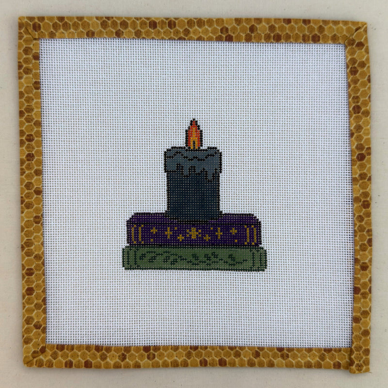 Hand-painted needlepoint canvas of a lit black candle on a stack of spellbooks