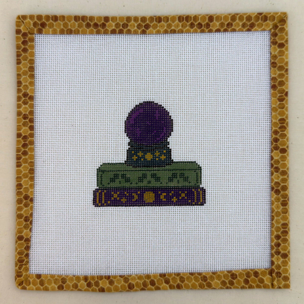 Hand-painted needlepoint canvas of a purple crystal ball on a stack of spellbooks