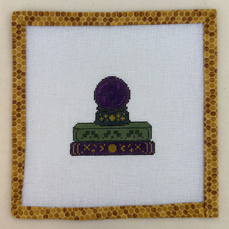 Hand-painted needlepoint canvas of a purple crystal ball on a stack of spellbooks