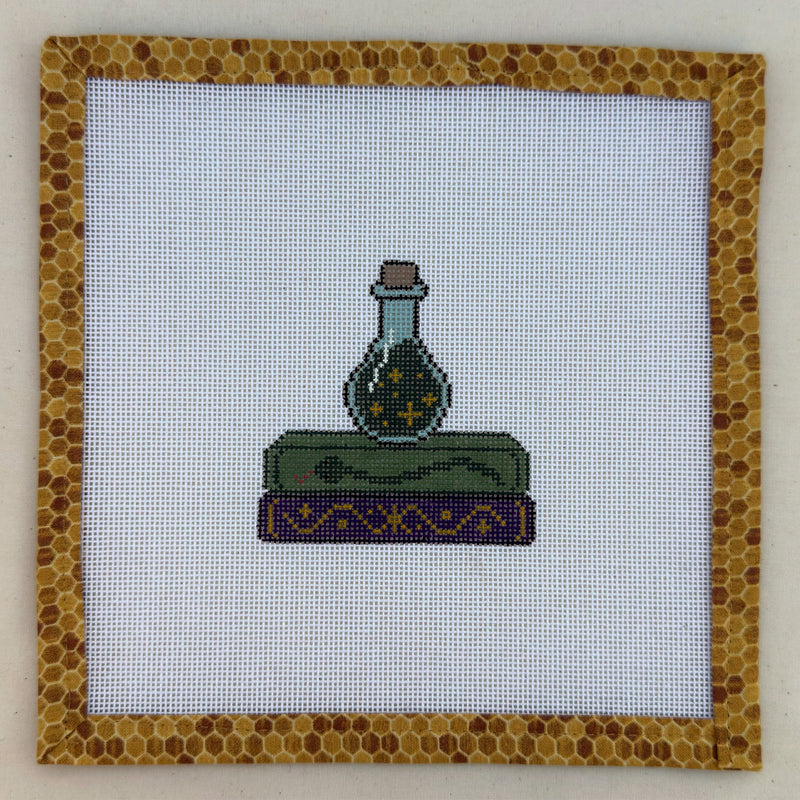 Hand-painted needlepoint canvas of a green potion bottle on stacked spellbooks